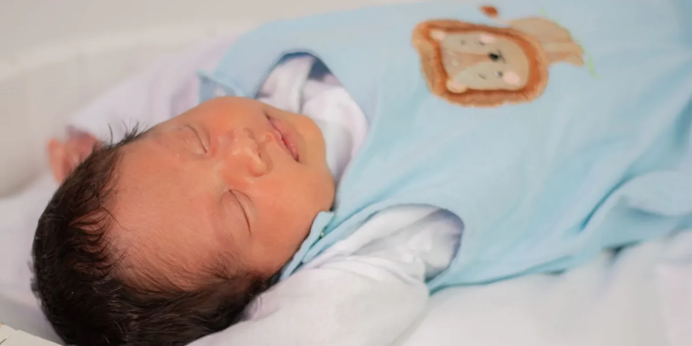Baby slaapt op de rug in een baby slaapzak in het ledikantje