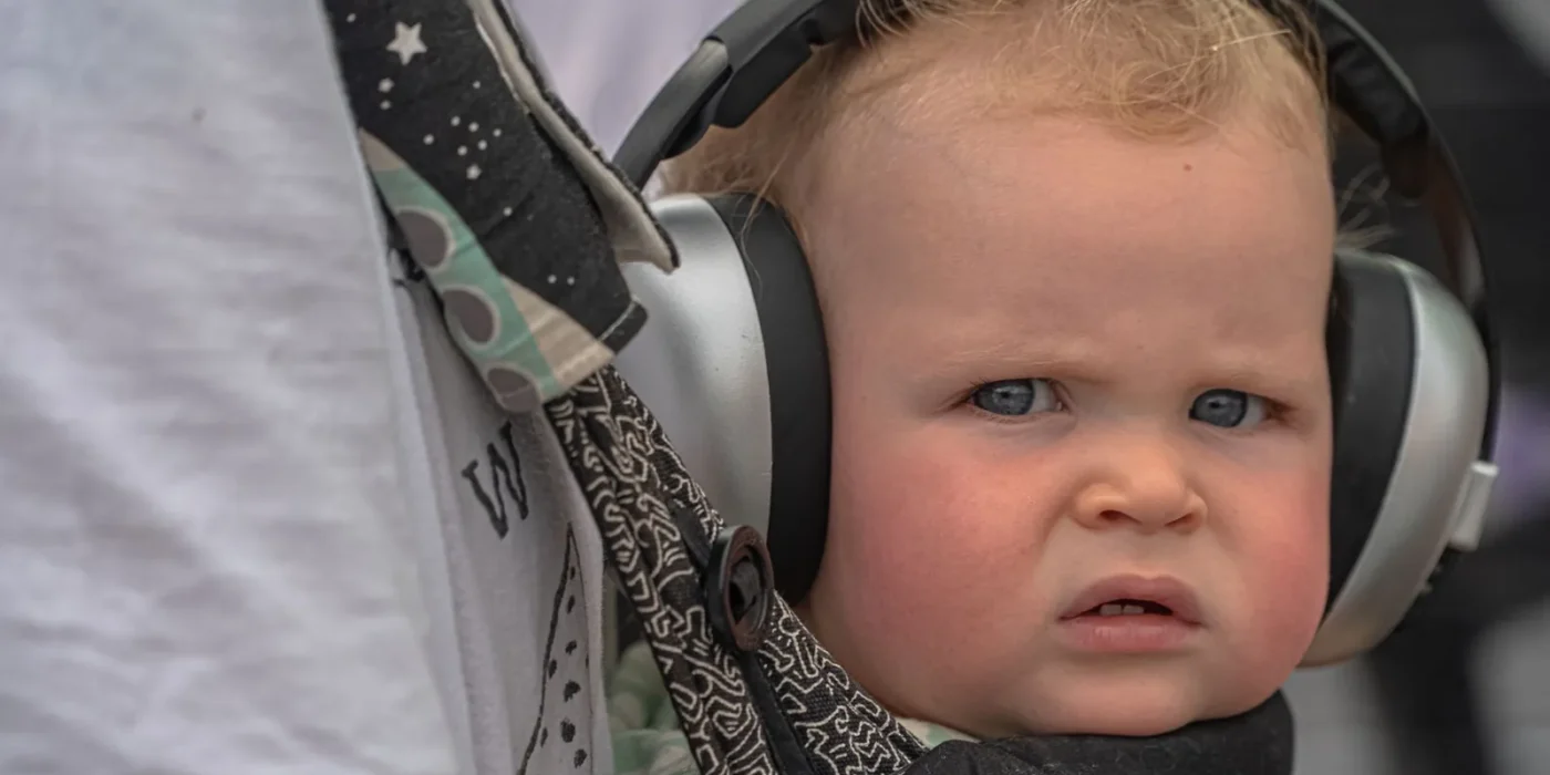 Baby met gehoorbescherming baby-oorkappen buiten bij een evenement