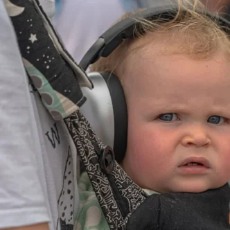 Baby met gehoorbescherming baby-oorkappen buiten bij een evenement