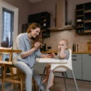 Moeder geeft haar baby een hapje in de kinderstoel volgens het voedingsschema baby