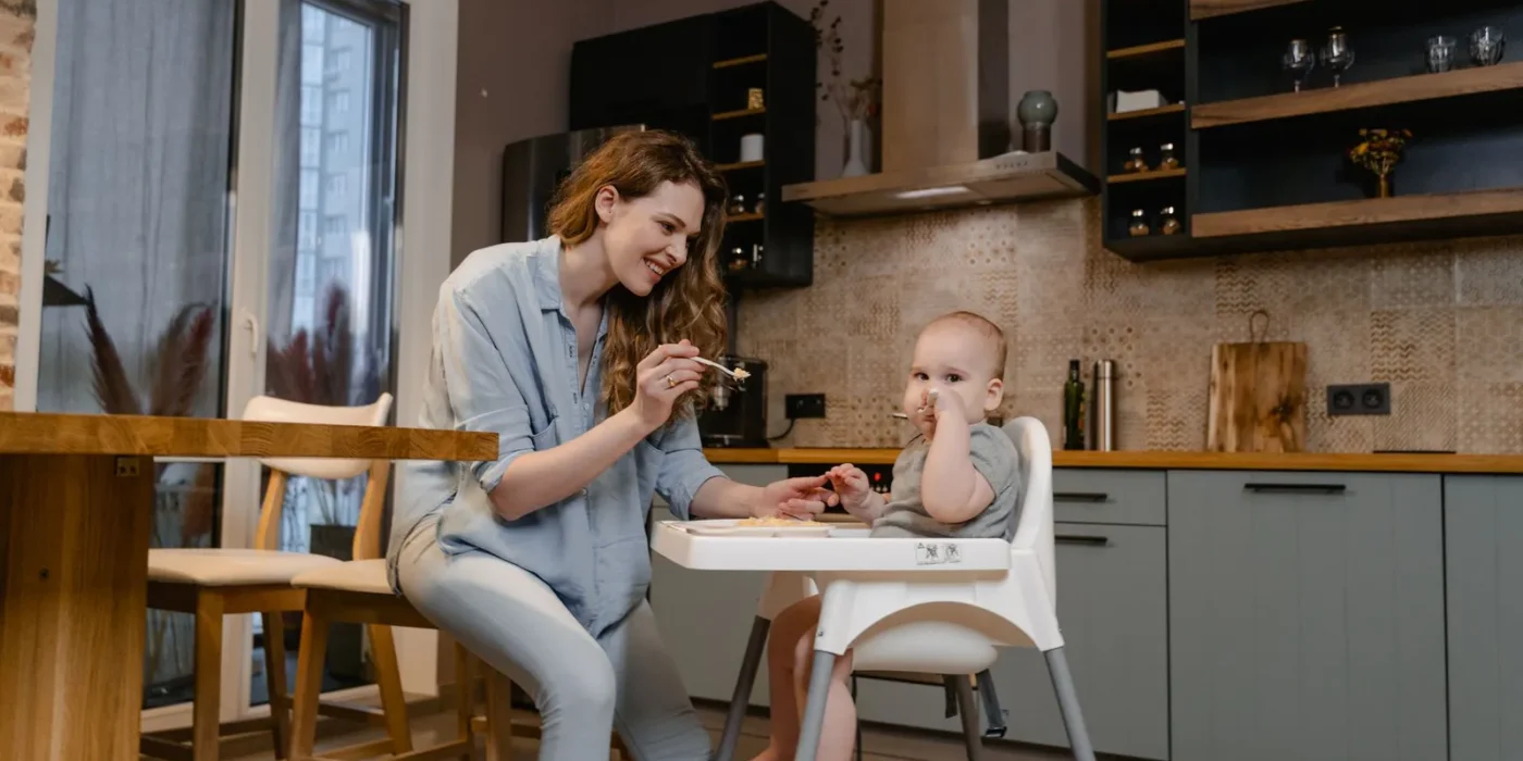 Moeder geeft haar baby een hapje in de kinderstoel volgens het voedingsschema baby