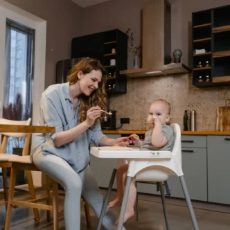 Moeder geeft haar baby een hapje in de kinderstoel volgens het voedingsschema baby